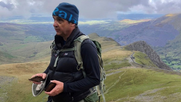 Image shows a man walking in a mountain setting.