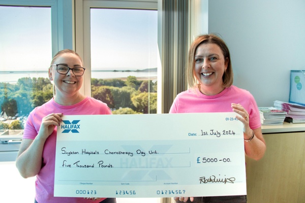 Two smiling women in pink t-shirts holding up a cheque