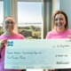 Two smiling women in pink t-shirts holding up a cheque