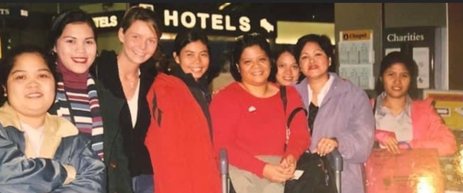 A group of Fillipino nurses stand shoulder to shoulder smiling at the camera 