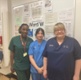 Three women wearing scrubs stood on a hospital ward
