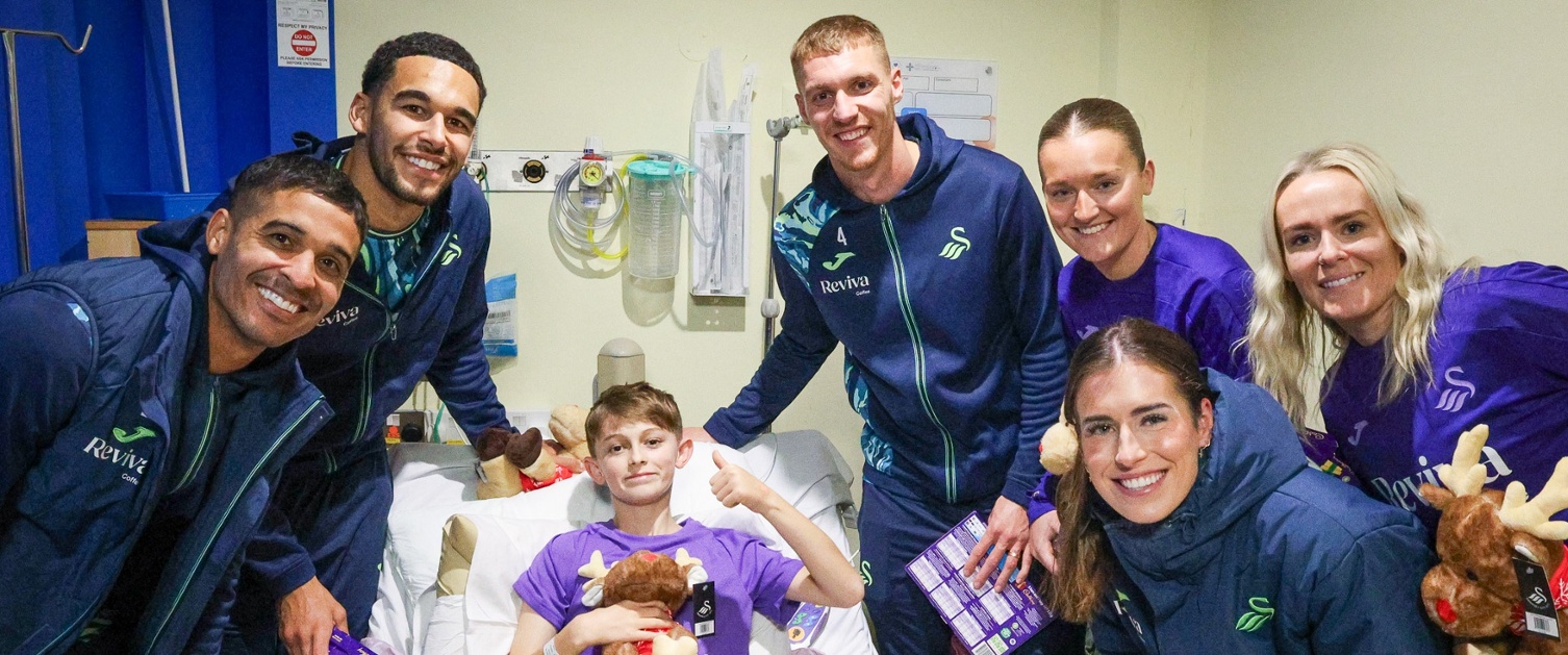 Image shows a group of people stood around a child in a hospital bed