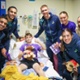 Image shows a group of people stood around a child in a hospital bed