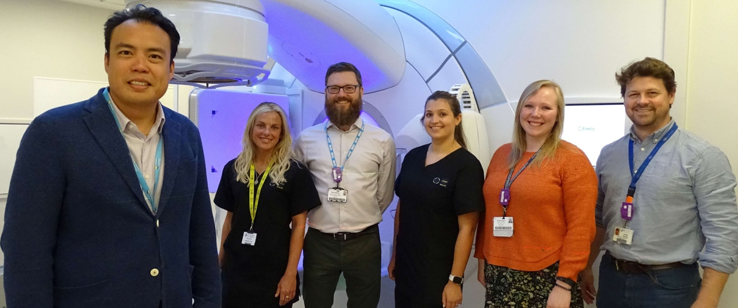 Image shows a group of clinicians standing in a radiotherapy treatment room