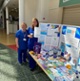 Two nurses stand next to a table displaying leaflets.