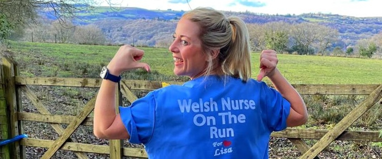 A nurse in scrubs pointing to lettering on her uniform