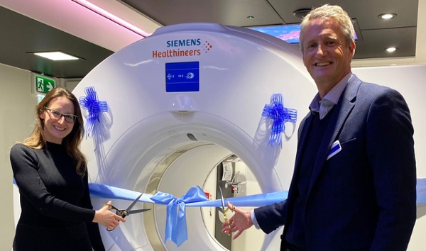 Image shows two people cutting a ribbon in front of a medical scanning machine.