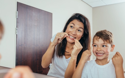 A woman standing next to a young boy flossing their teeth