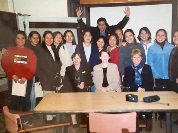 A group of Fillipino nurses stand shoulder to shoulder smiling at the camera 