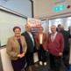 Image shows a group of people standing in front of a banner