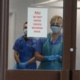 Image shows two clinical staff in face masks and face shields looking out 