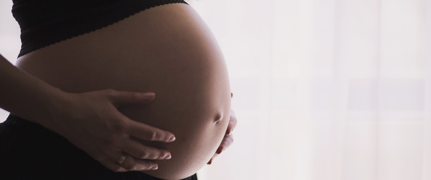 A pregnant woman with her hands on her stomach.