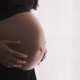 A pregnant woman with her hands on her stomach.