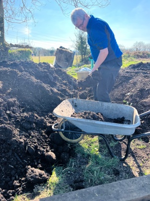 Image shows a man shovelling compost into a wheelbarrow