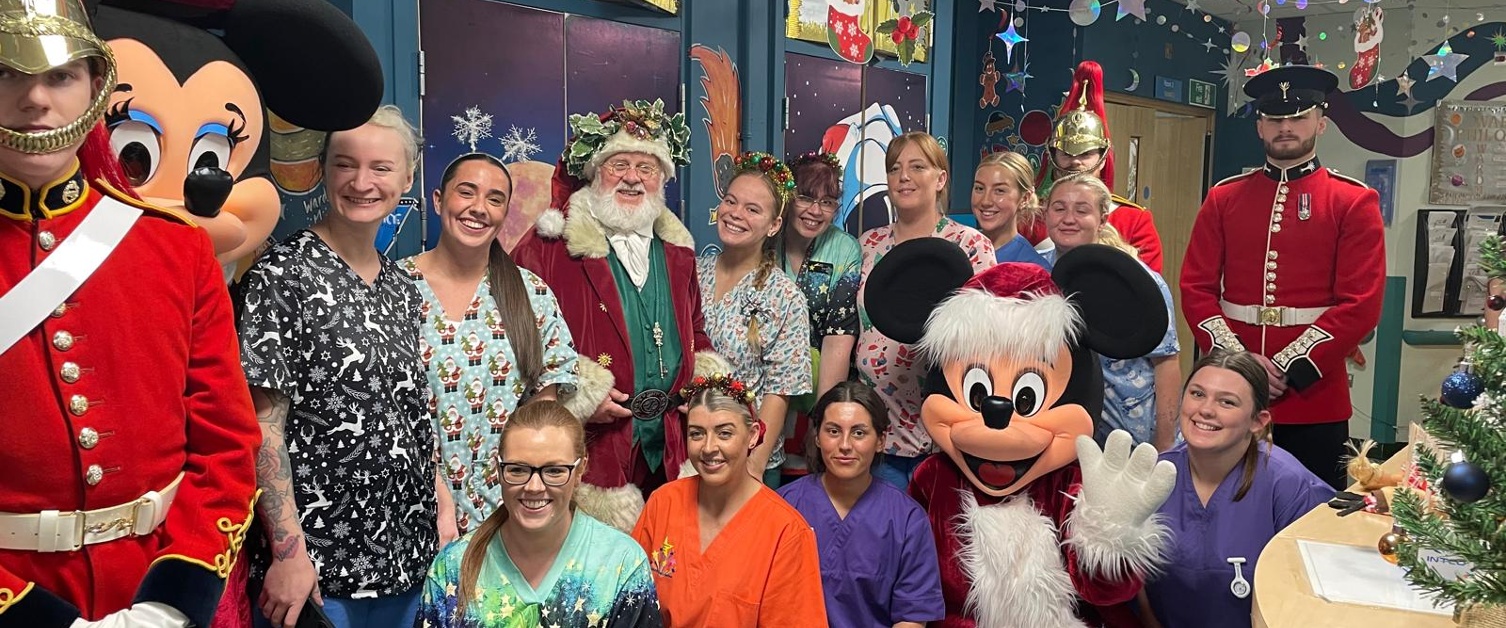 Santa, hospital staff, soldiers and Mickey Mouse smiling in a hospital ward