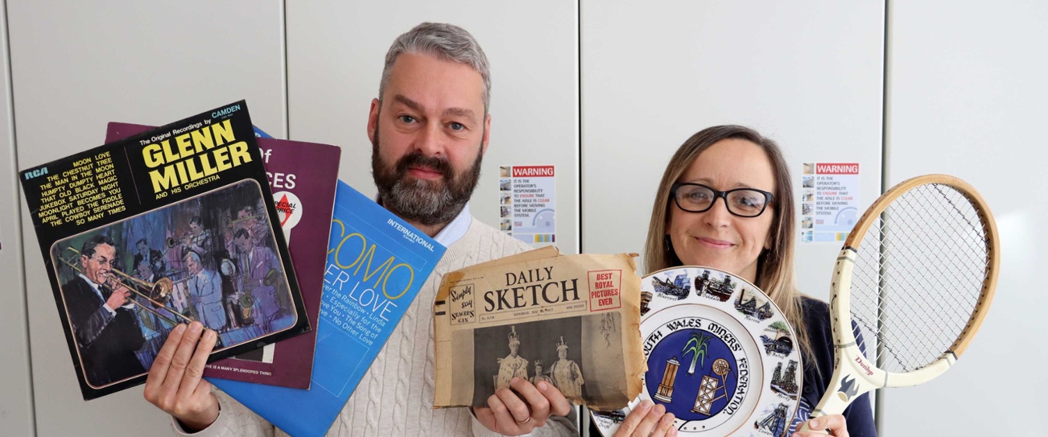 Library staff hold up old vinyl albums, a copy of the Daily Sketch newspaper from the Queen