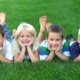 Four young children laying on grass smiling at the camera