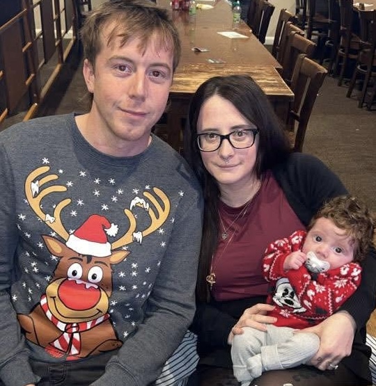 Image of a baby boy with his parents at Christmas.