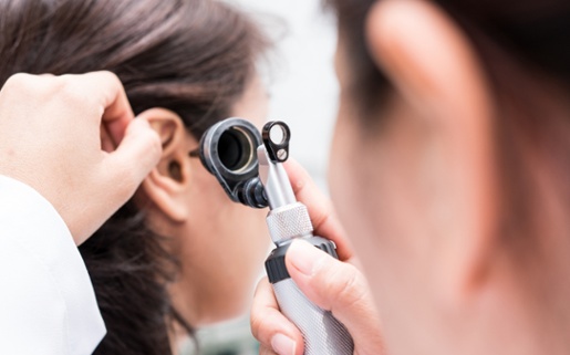 Image shows Audiologist examining a patients ear.