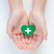 Image shows hands and wrists. Open hands hold a green heart.