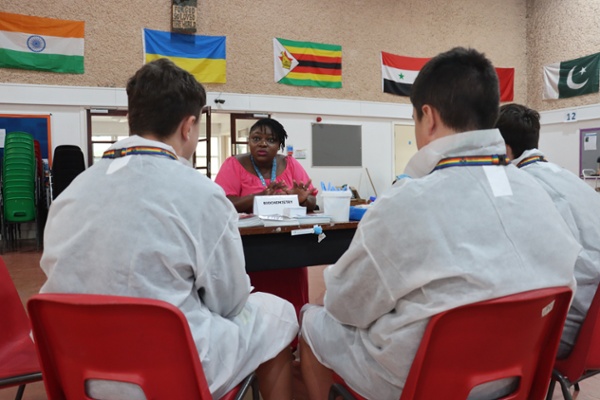 Two school children dressed in lab coats talking to a scientist