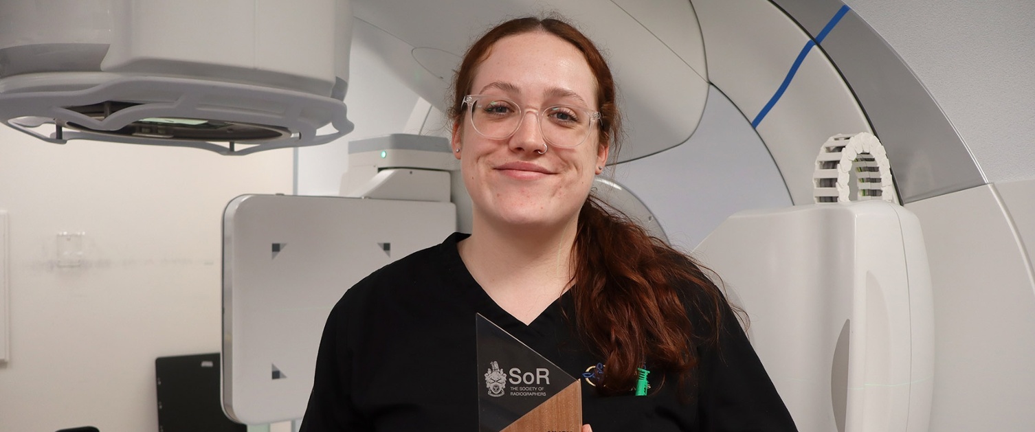 Image shows a smiling woman holding an award.
