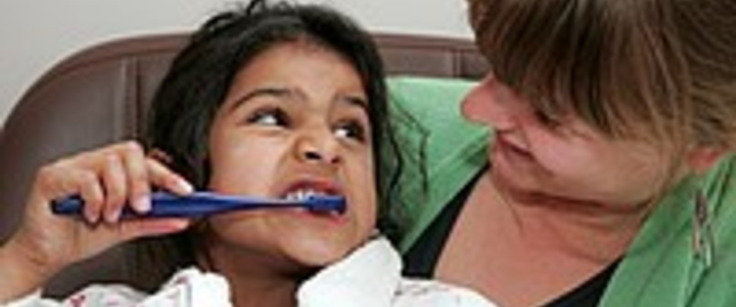 A young girl brushing her teeth while her mother watches