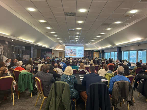 A photo of attendees sat at tables viewing a presentation on a screen
