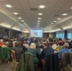 A photo of attendees sat at tables viewing a presentation on a screen