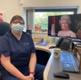 A woman wearing a mask sat at a desk with a photo of the Queen on her screen