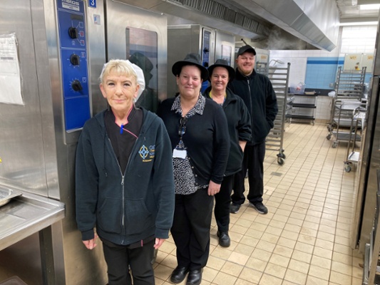 Image shows four people standing in a kitchen