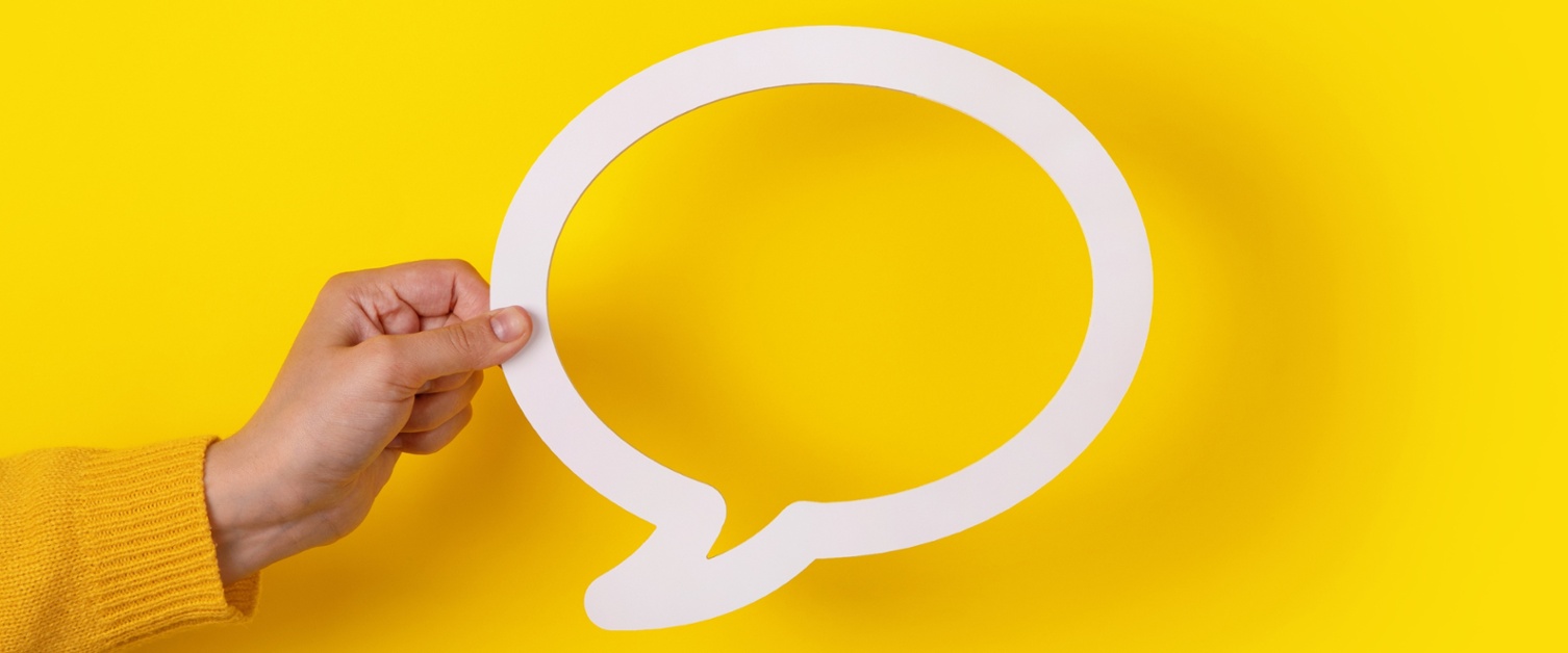 Image shows a hand holding up a white speech bubble in front of a yellow background.