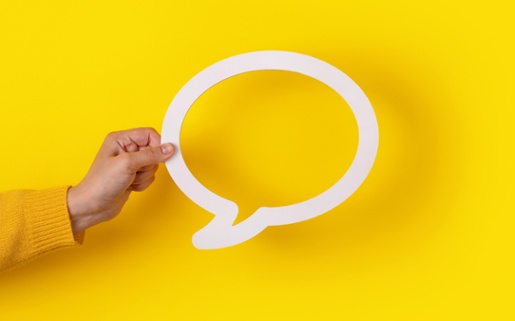 Image shows a hand holding up a white speech bubble in front of a yellow background.