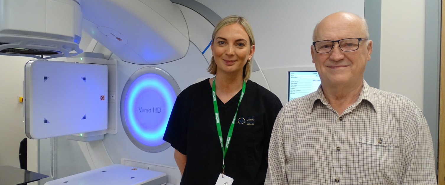 A smiling man, with a nurse standing just behind him in a hospital treatment room