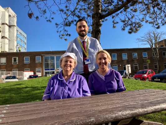 Image shows a man and two women behind a bench