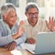 Older couple on a video call on a laptop are waving.