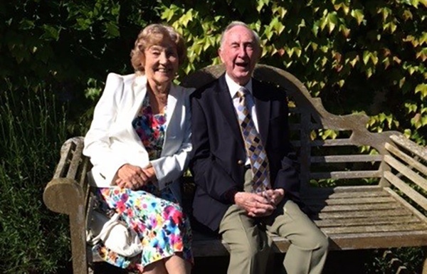 Image shows an elderly couple sitting on a bench.