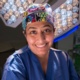 Professor Bhatti is pictured in an operating theatre in scrubs smiling.