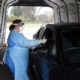A nurse in protective clothing swabs mouth of a man in a car at testing unit