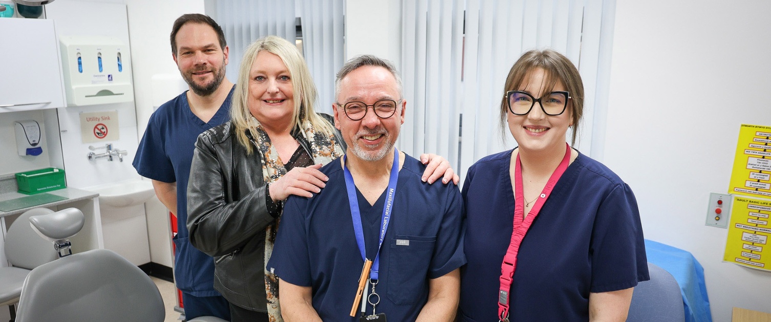 Image shows three clinicians and a patient in a hospital room.