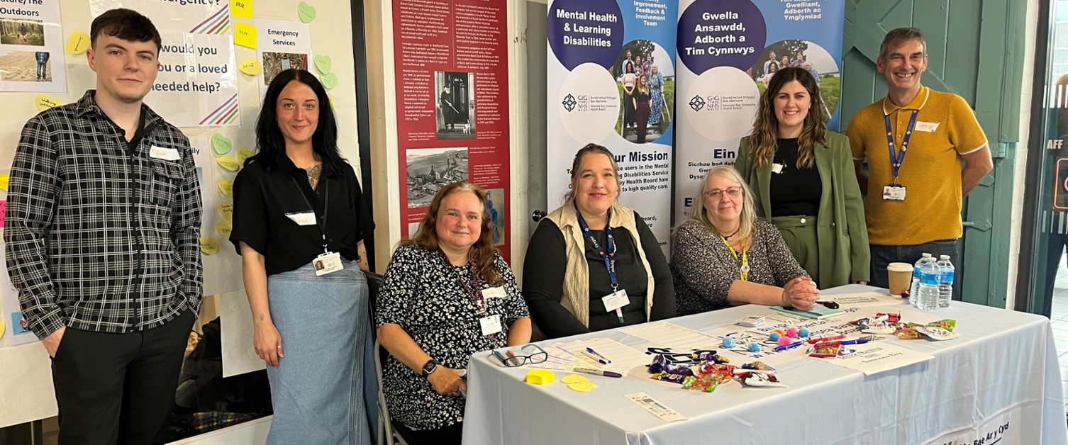 Image shows a woman and man group of people standing next to a table display