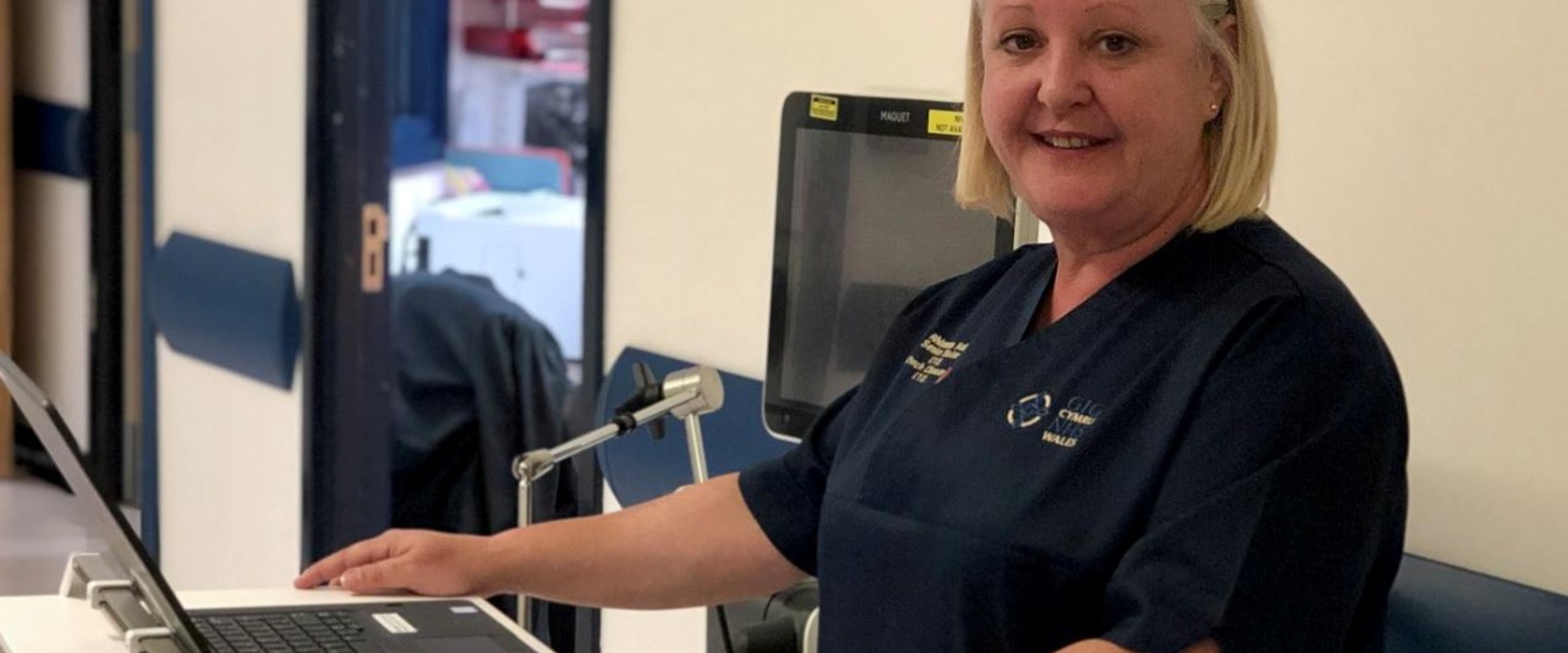 A nurse in a dark blue uniform stands smiling as she stands in front of a laptop on top of a mobile work unit.