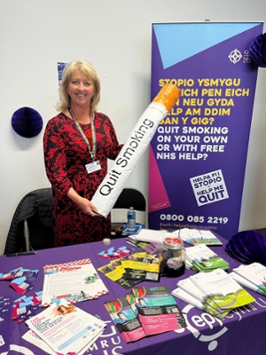 Image shows a woman holding an inflatable cigarette next to a table display
