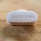 Image shows a single white tablet inscribed with word Amitriptyline.