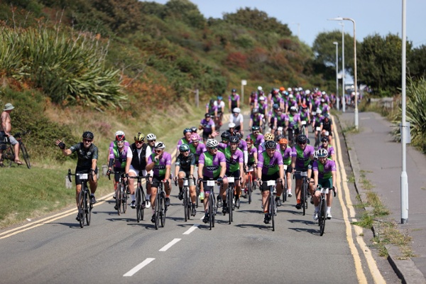 A large group of cyclists riding down a road in the sunshine