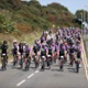 A large group of cyclists riding down a road in the sunshine