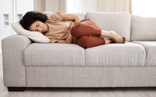 A woman laying on a sofa clutching her stomach