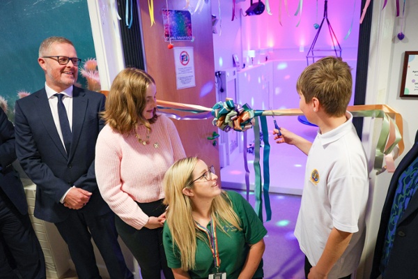 A boy pictured cutting a ribbon while a nurse, a little girl and a man in a suit look on