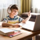 Image shows young boy sat in front of laptop smiling and holding up his thumb.