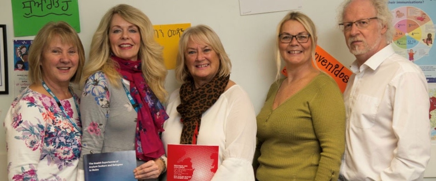 A group of health board staff smile at the camera. They are holding printed copies of research papers which their work directly fed into.